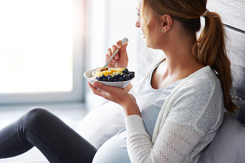 Side view of pregnant woman having breakfast at bedroom