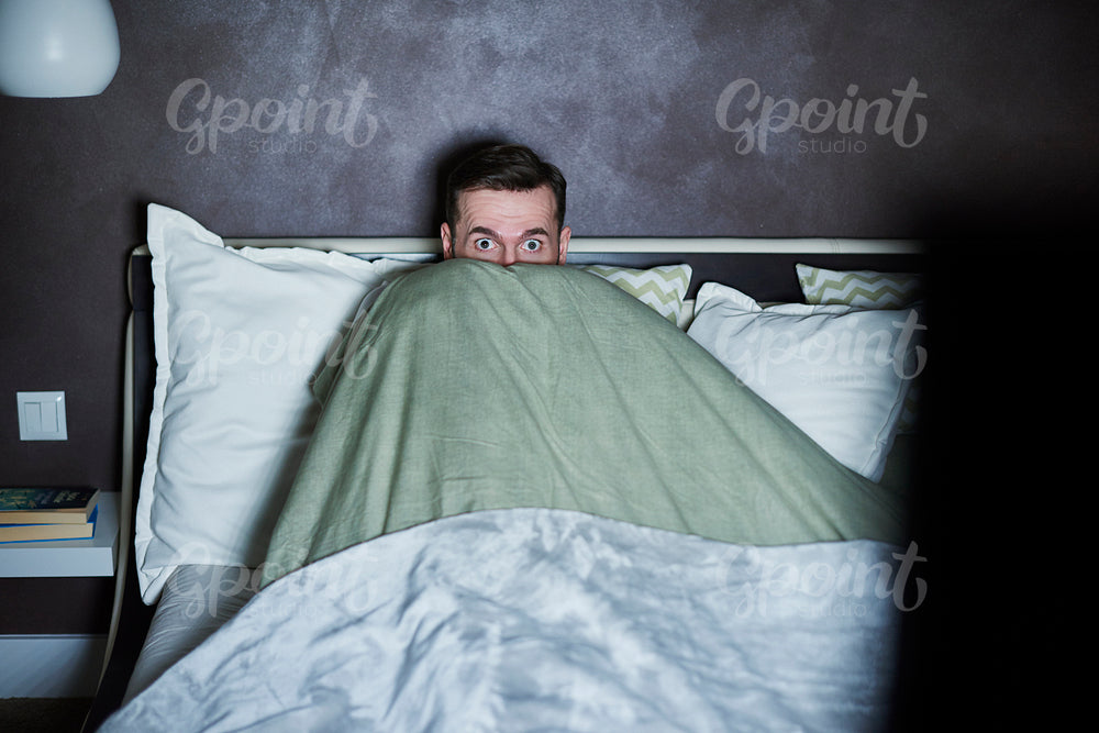 Scared man watching horror movies in bed