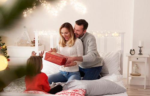 Excited family with gift spending Christmas morning in bed