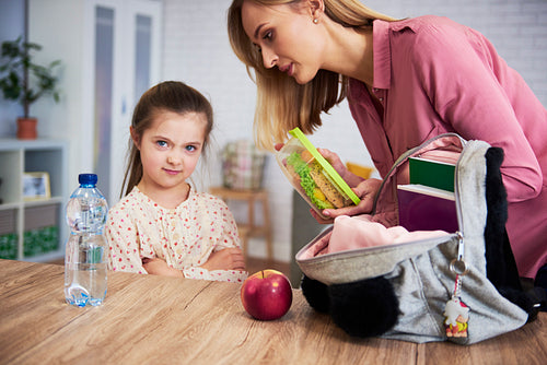 Mother putting lunch box with healthy food in daughter's backpack