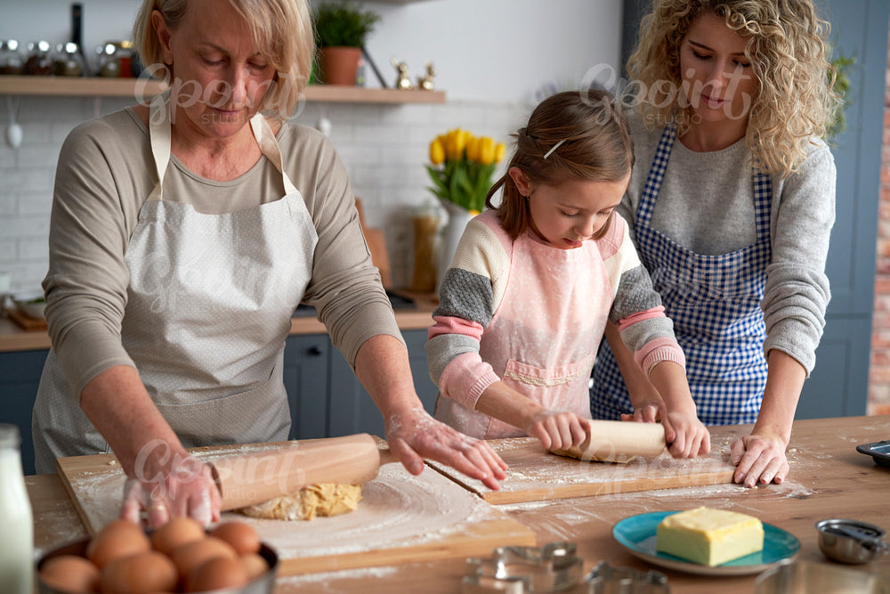 Three generations of women rolling dough together at home