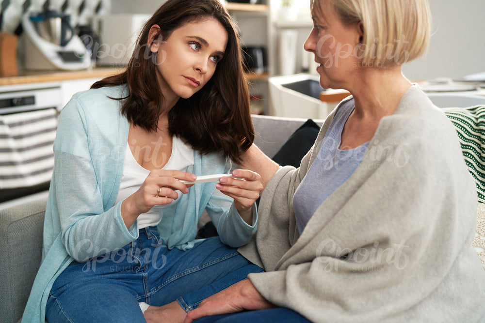 Sad woman holding negative pregnancy test with a supportive mother
