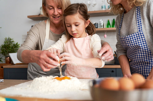 Little girl with grandmother breaking an egg into the flour