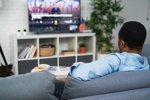 Rear view of black man watching USA election on TV