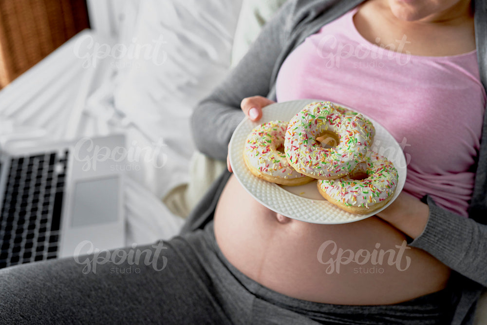 Top view of pregnant woman with few donuts on plate