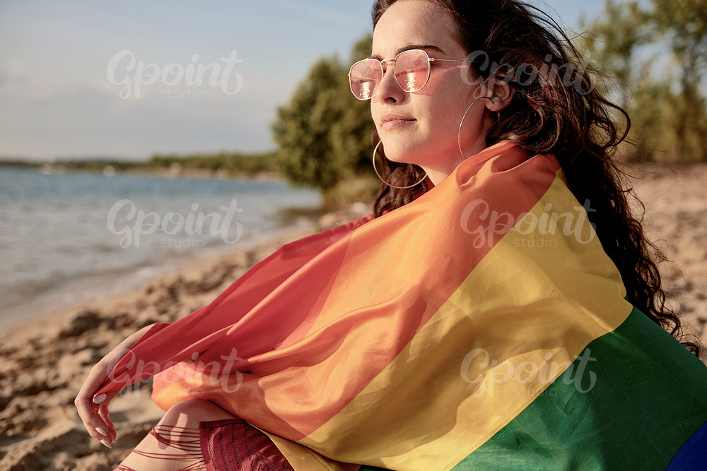 Young woman wrapped in rainbow flag on the beach
