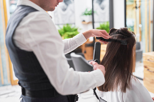 Close up of hairdresser using comb and straightener