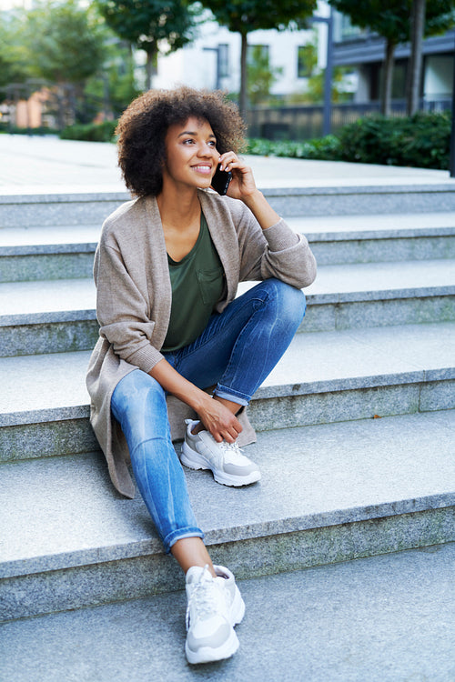 Smiling woman sitting on city steps with the mobile phone
