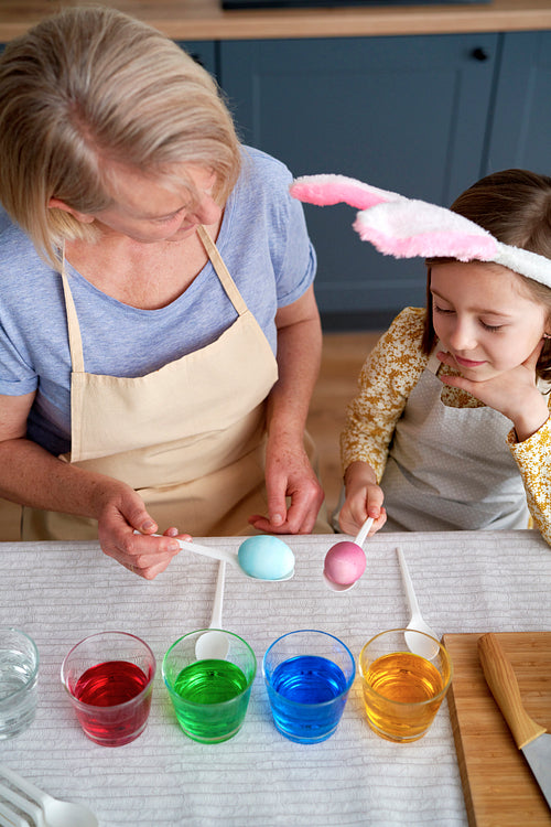 Top view of grandmother and granddaughter dyeing Easter eggs together