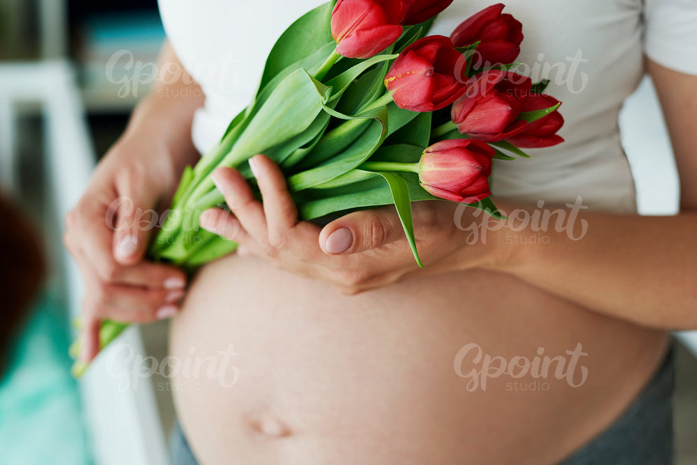 Close up of human pregnant abdomen and bunch of flowers