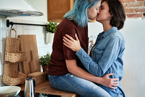 Romantic lesbian couple kissing and hugging intimately in the kitchen