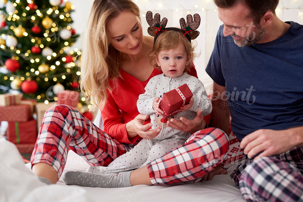 Baby opening Christmas gift with parents in bed