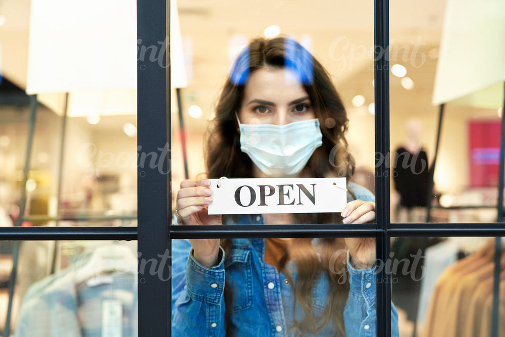 Front view of woman in protective mask holding open sign