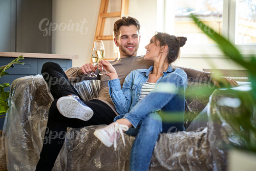 Happy caucasian couple celebrating house purchase while sitting on sofa and drinking champagne