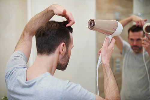Rear view of man drying his hair in bathroom