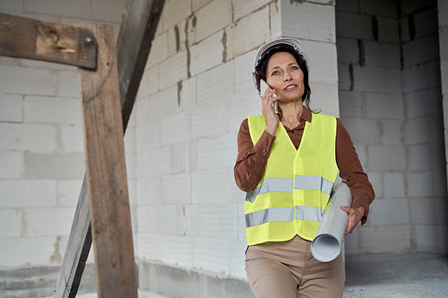 Female mature caucasian engineer moving on the stairs on construction site and talking one mobile phone