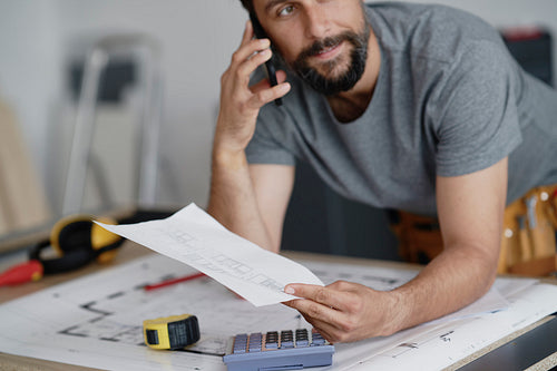 Carpenter holding plans and talking on the phone
