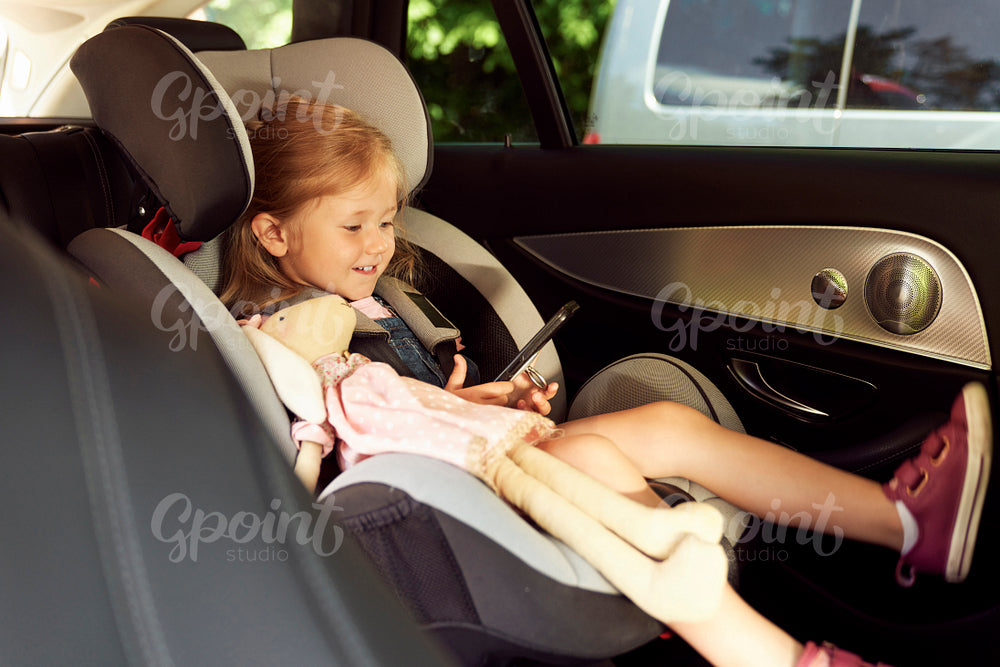 Cute girl sitting in baby car seat and using phone