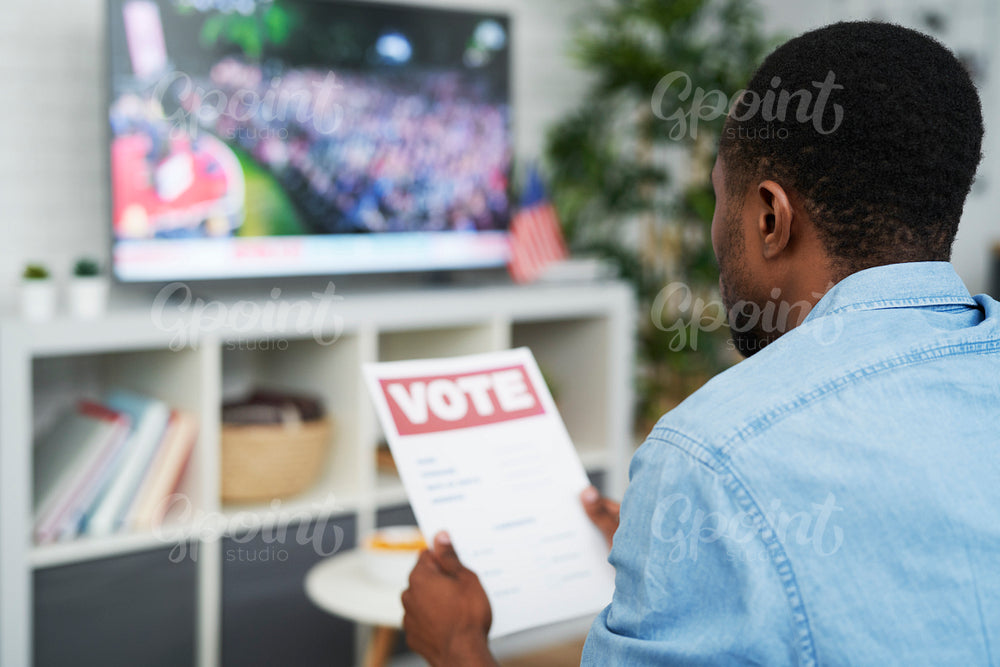 Pensive man watching tv and holding vote document