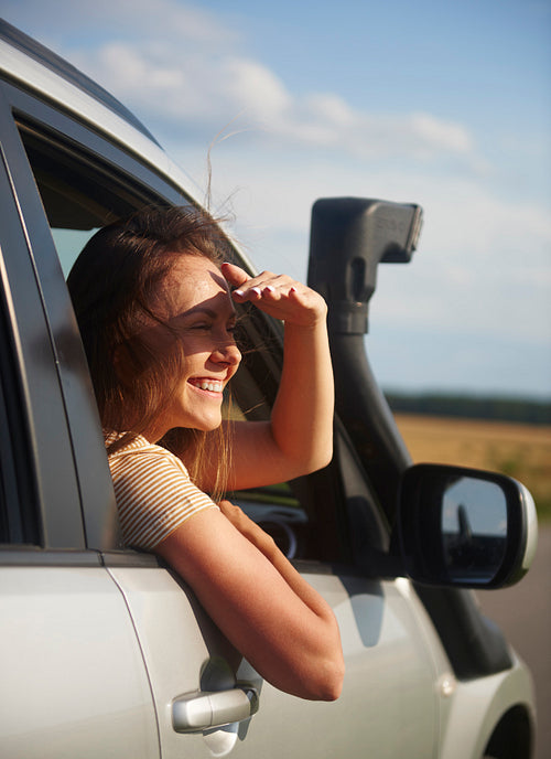 Happy young woman traveling by car and looking at view