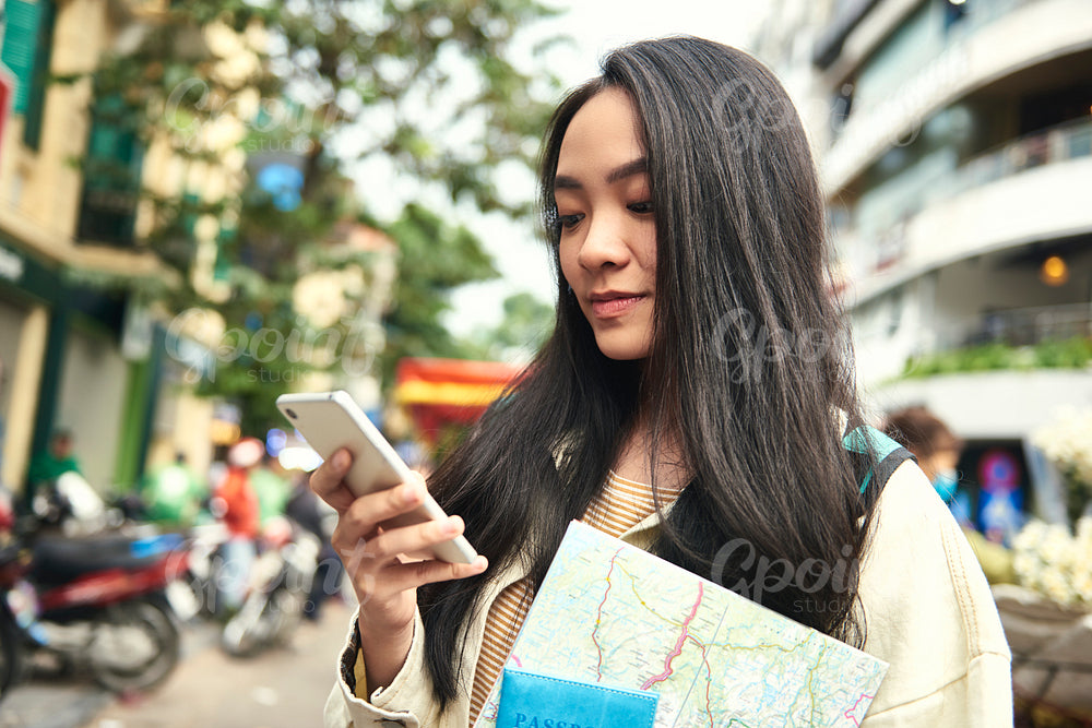Asian woman with passport and paper map using mobile phone