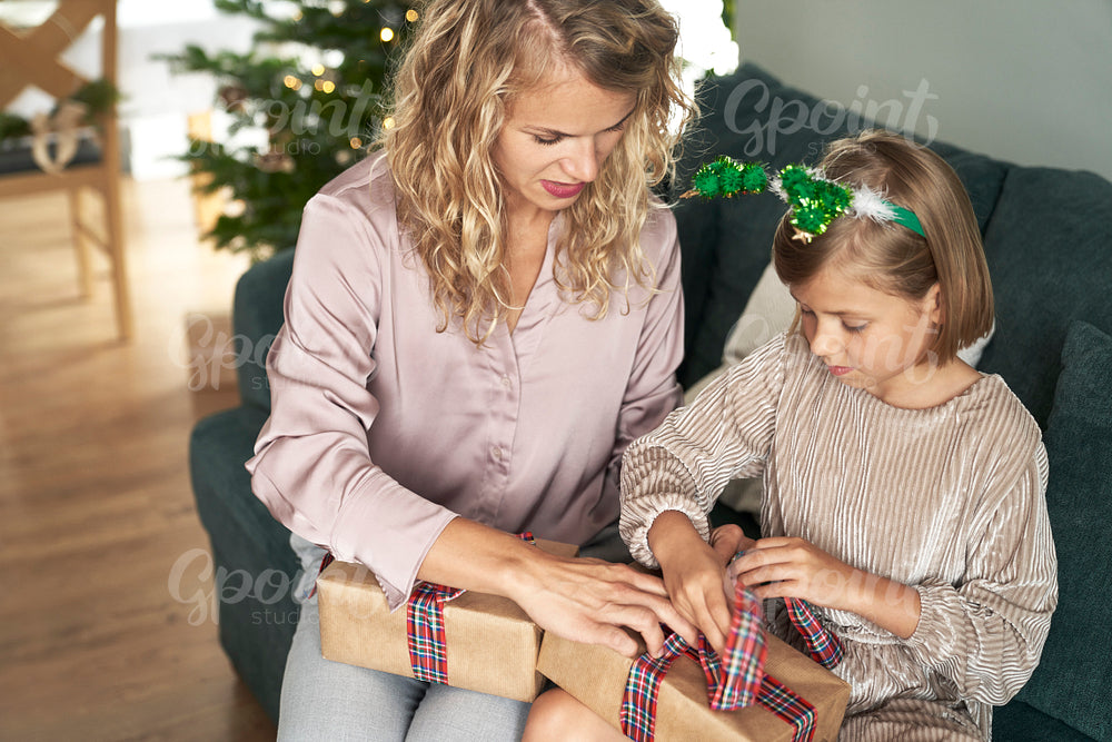 Caucasian girl and mother packing Christmas present  on sofa 