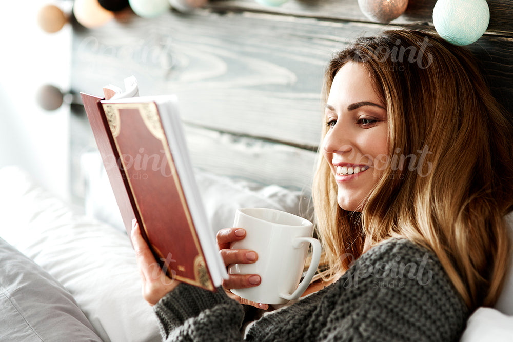 Woman with coffee reading book in bedroom