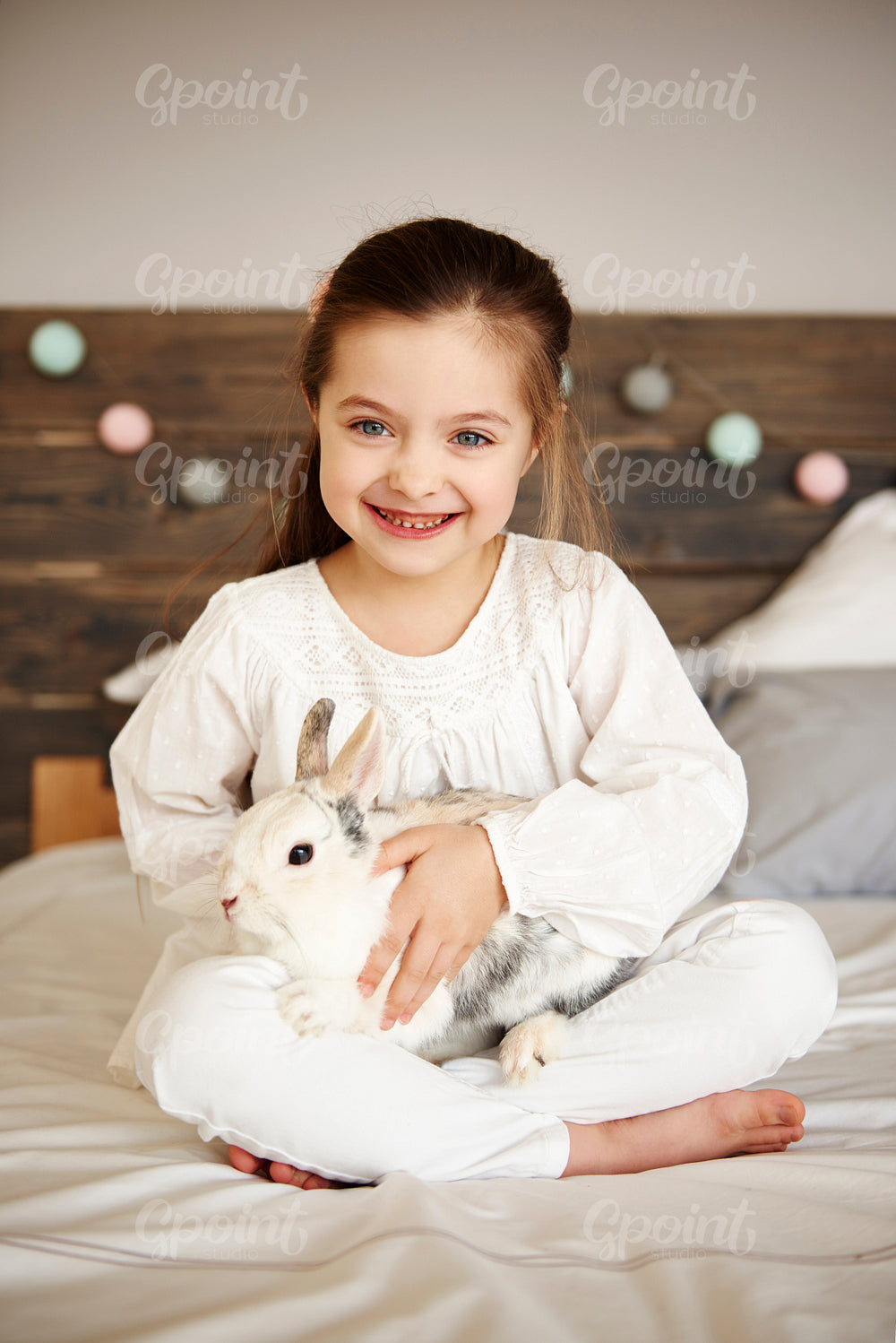 Smiling girl embracing her rabbit in bed