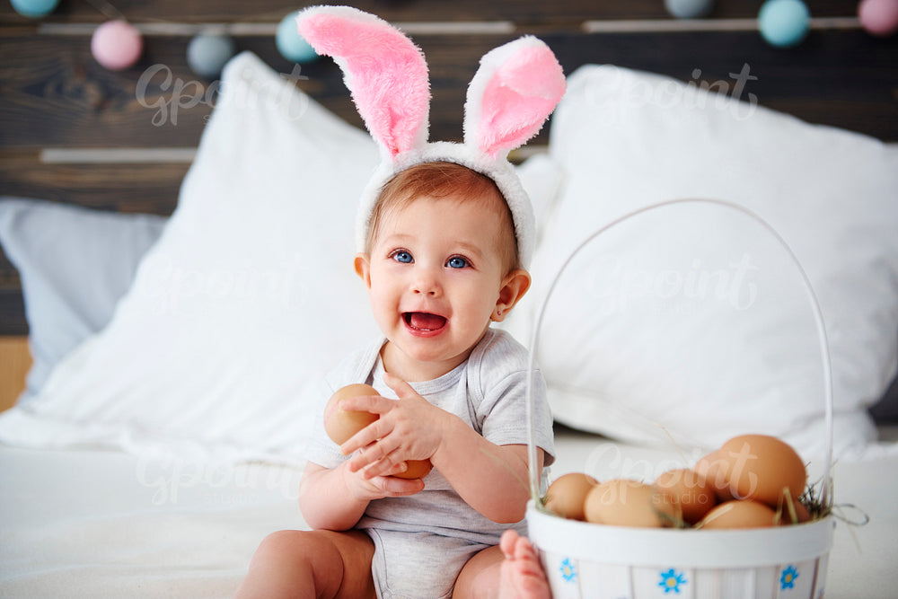 Portrait of baby with bunny ears holding eggs