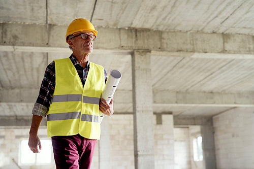 Senior man walking and holding plans on the construction site