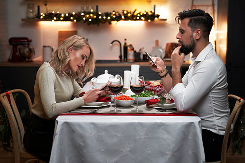 Front view of couple spending Christmas dinner on their phones