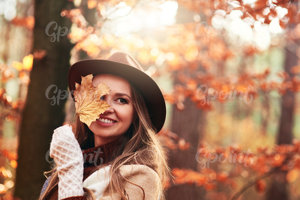 Happy beautiful woman  covering eye with autumnal leaves