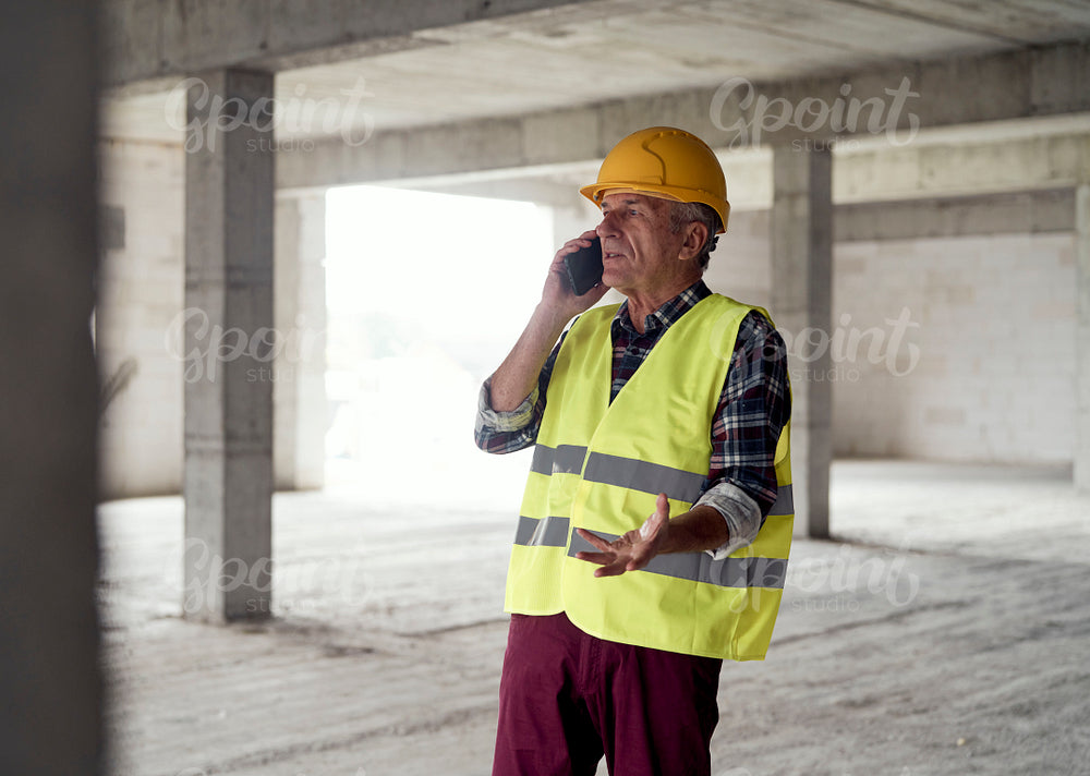 Senior caucasian man talking by mobile phone on the construction site 