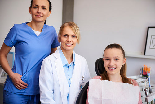 Portrait of two smiling orthodontists and child in dentist's office