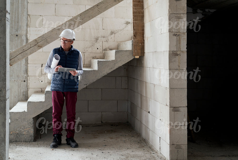 Caucasian senior engineer holding plans and digital tablet while standing on construction site     
