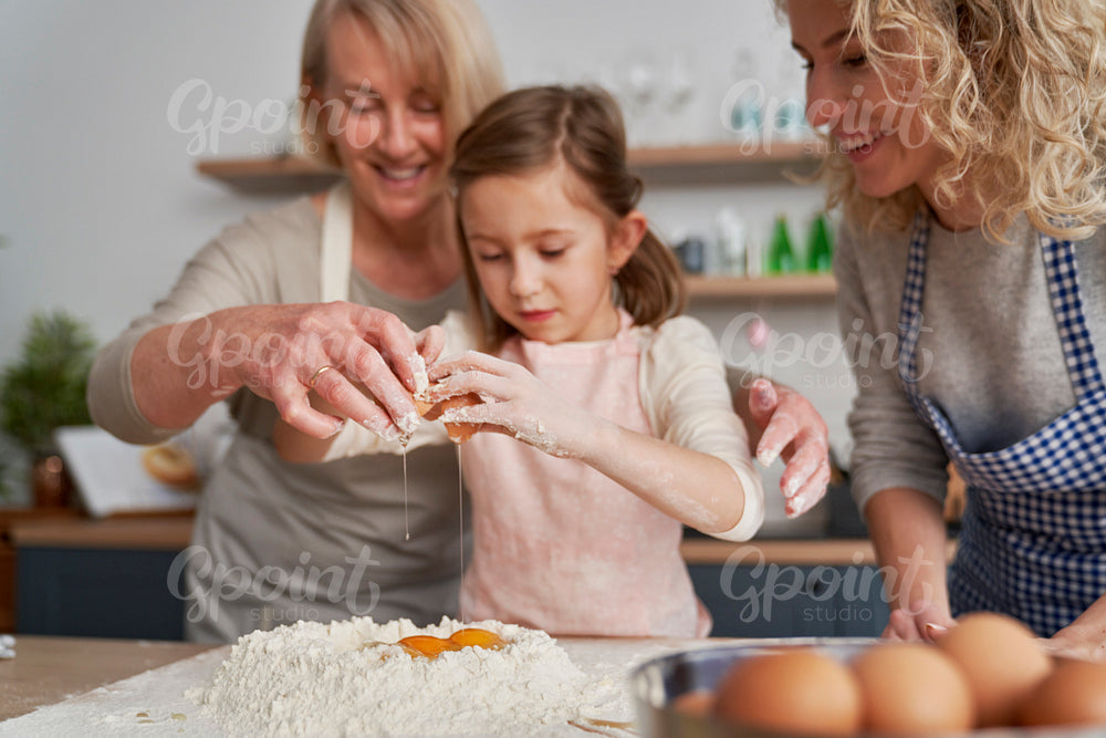 Little girl breaks an egg into the flour
