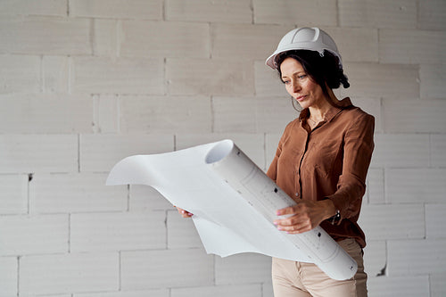 Female mature caucasian engineer standing on construction site and browsing building plans
