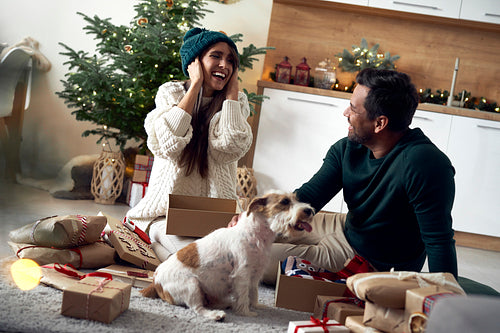 Happy couple opening Christmas presents with dog at home
