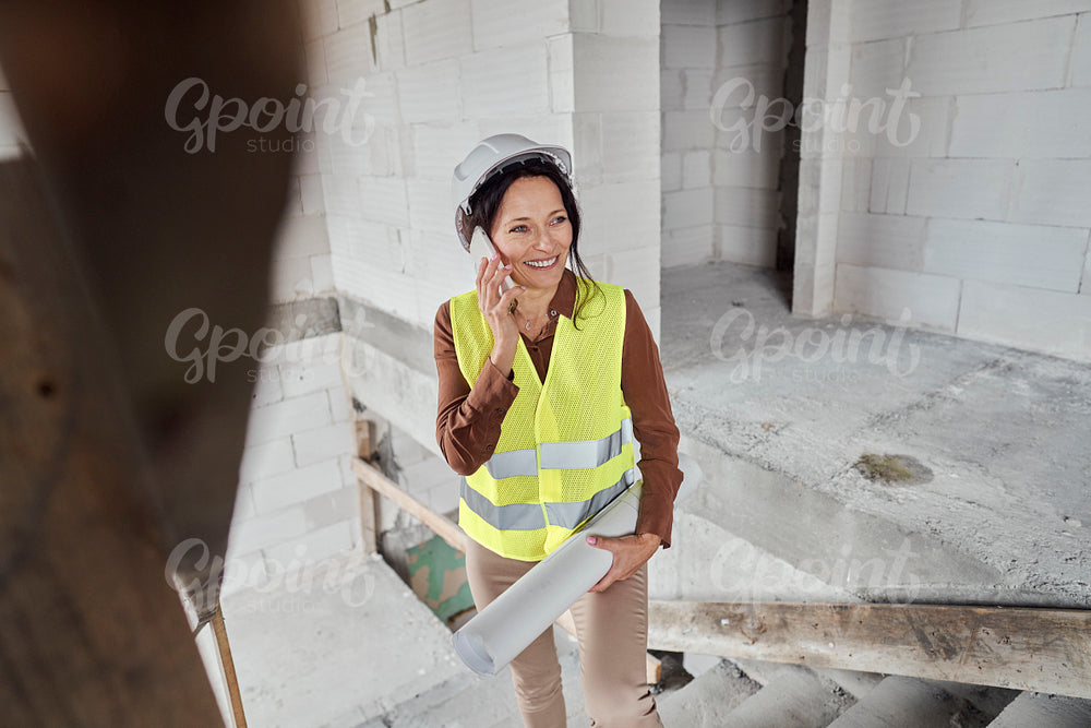 Female mature caucasian engineer standing on the stairs on construction site and talking on mobile phone 