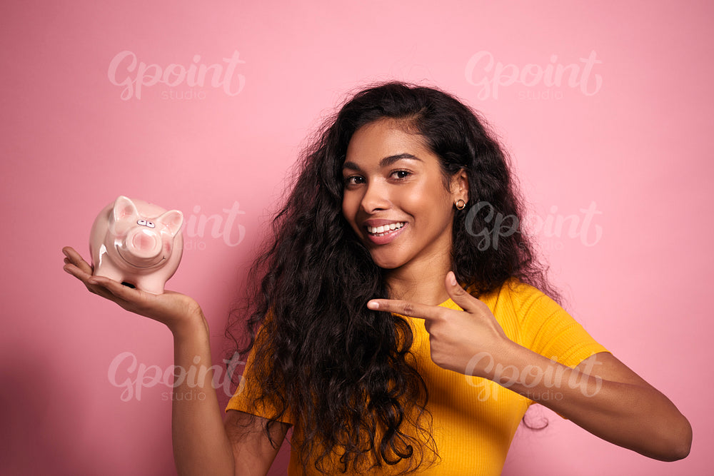 Smiling African woman pointing the piggy bank in studio shot.