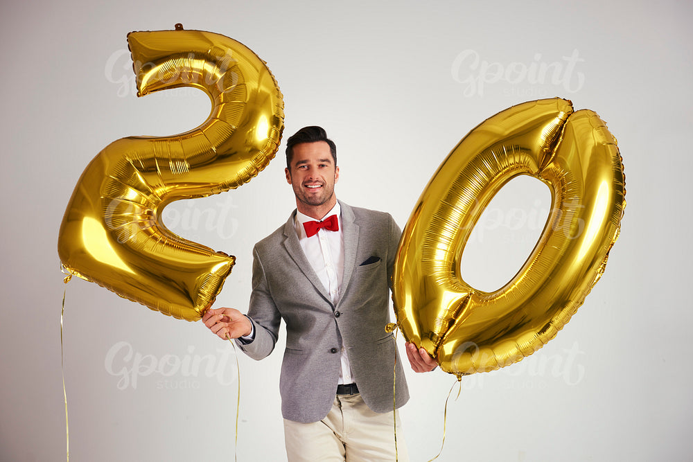 Young man with golden balloons building the figure "20"