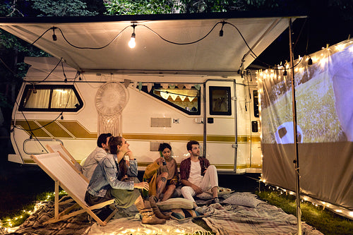 Young cheerful people watching a movie at camping site