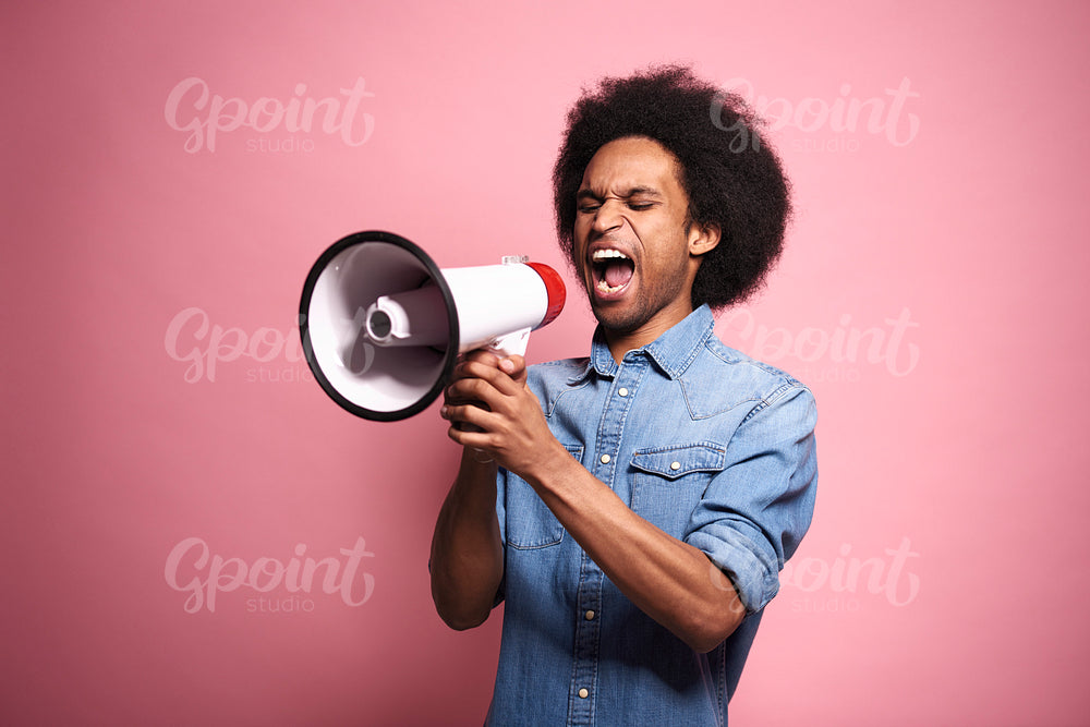 Young African man shouting into a megaphone in studio shot.