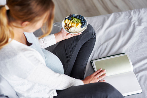 Top view of pregnant woman eating and reading a book