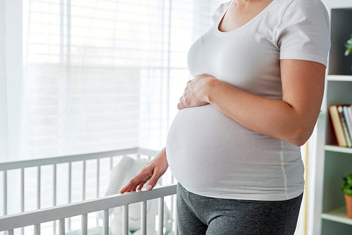Pregnant woman standing next to a baby crib