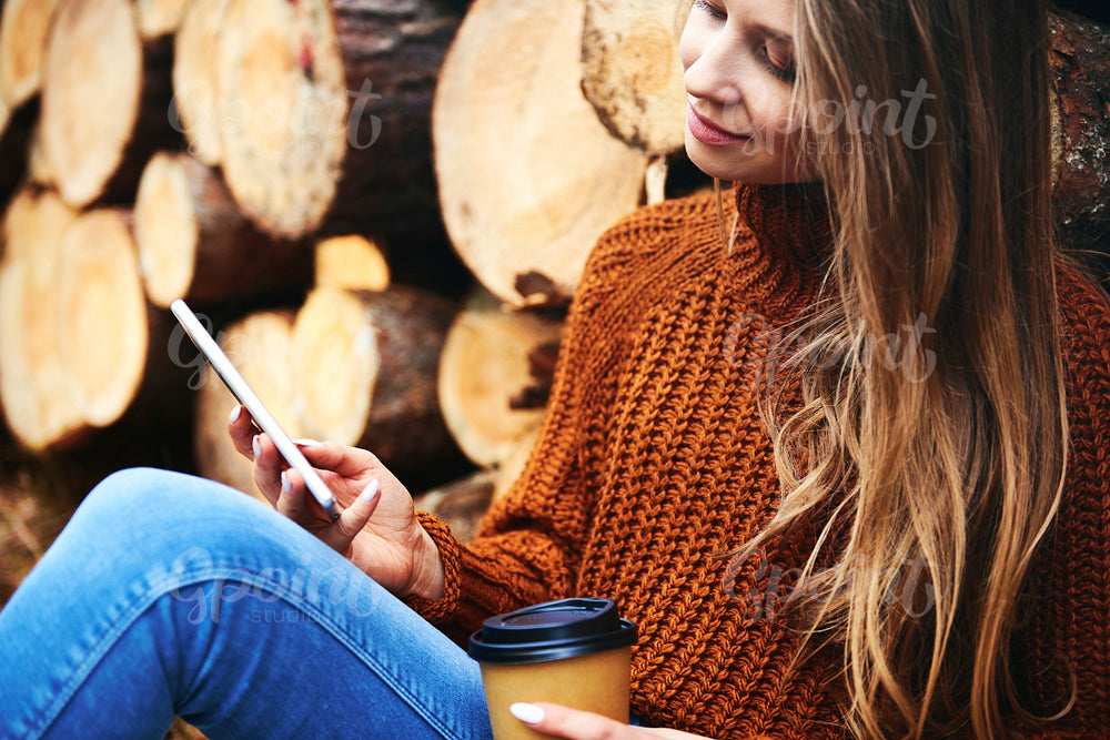 Woman relaxing with coffee cup and phone in autumnal forest