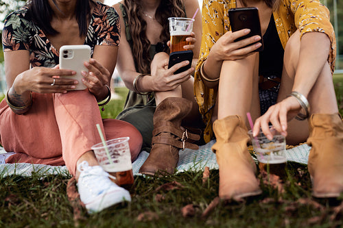Low section of women sitting on the grass and holding mobile phones