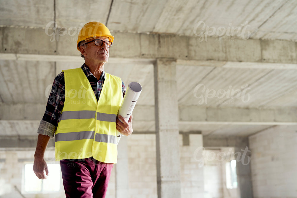 Senior man walking and holding plans on the construction site 