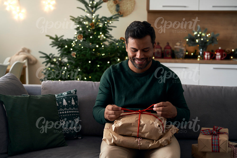 Latino man with Christmas present sitting on sofa at home 