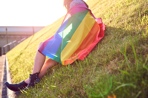Unrecognizable woman with a rainbow flag sitting on the grass